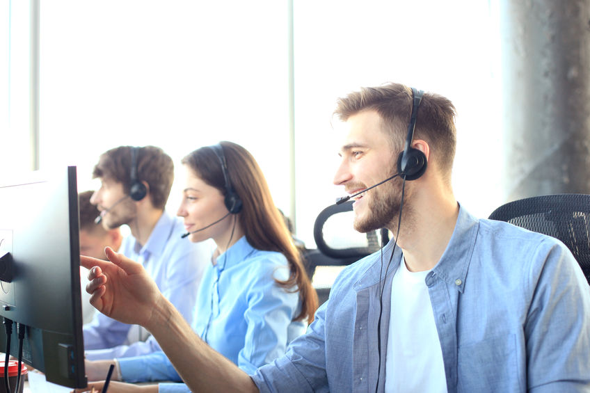 Portrait of call center worker accompanied by his team. Smiling customer support operator at work